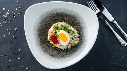 Salad Olivier from boiled vegetables and sausage with mayonnaise with egg, red caviar and microgreens on plate.