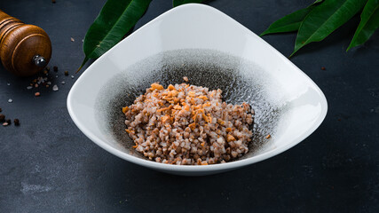 Garnish boiled buckwheat porridge with fried onions in a plate.