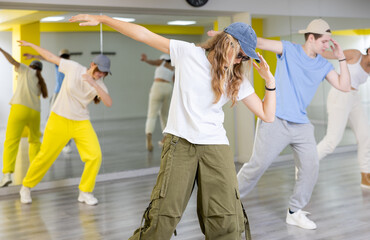 Teen girl in cap rehearses modern dances in dance hall