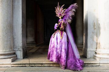 Fototapeta na wymiar Venice, Veneto, Italy - February 17th, 2023 - Beautiful colored carnival costume on the street in Venice. Carnival of Venice. Woman in purple dress.