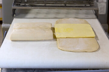 Baker in gloves working with raw dough and buttering the layers. Process of making homemade pastry