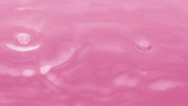 Macro crane shot of water drops drip on water surface creating water circles on pink background | Skin hydration concept