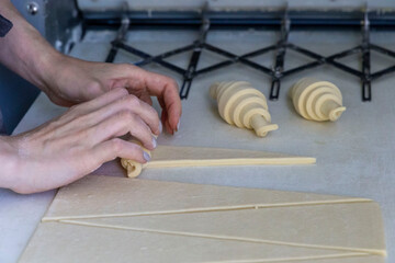 Woman rolls the dough into a croissant on the table one by one. Homemade pastry croissants baking