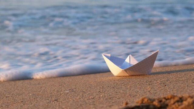 Paper boat waves crash on shore. A paper boat floating under sea waves on the sunny shore. A concept of summer resort and problems with trips by the water.