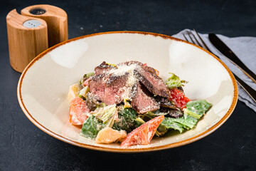 Meat salad with beef slices, tomatoes, parmesan cheese, pickled cucumber, lettuce and sauce.