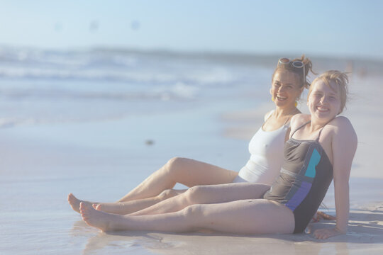 smiling stylish mother and child sitting at beach
