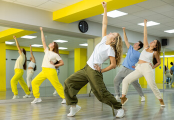 Trendy teenagers dancing hip-hop in studio, learn dance moves together, wearing stylish outfit