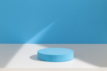 Round podium for products or cosmetics against blue pastel background with geometric shadows.	
