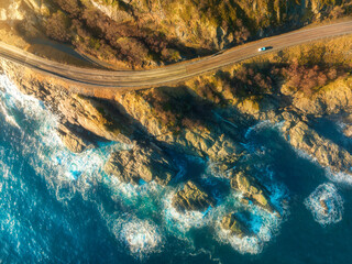 Aerial view of road, rocky sea coast with waves and stones at sunset in Lofoten Islands, Norway. Landscape with beautiful road, transparent blue water, rocks. Top view from drone of highway in summer - obrazy, fototapety, plakaty
