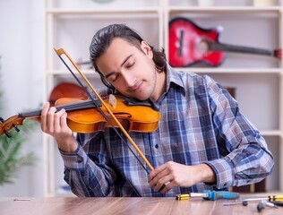 Young handsome repairman repairing violin