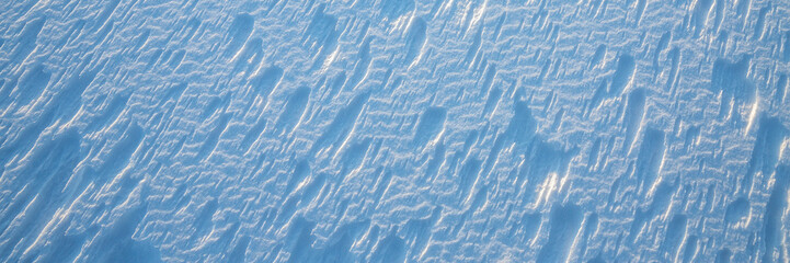 Beautiful winter background with snowy ground. Natural snow texture. Wind sculpted patterns on snow surface. Wide panoramic texture for background and design.