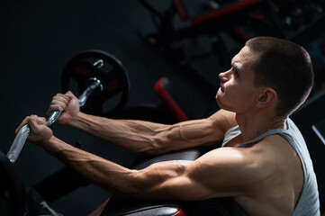 Man doing EZ barbell bicep exercises on Scott bench. 