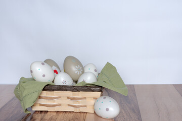 Decorated Easter eggs in a basket on a wooden background and white wall.