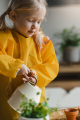 Little cute blonde child girl is watering and care of indoor plants. Transplants flowers. Home gardening concept. Earth Day. A little helper in the household. vertical photo 