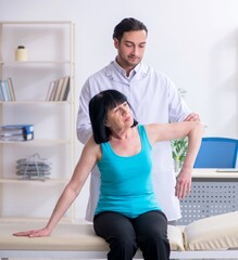 Young male doctor examining old female patient