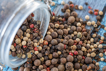 An upturned glass jar on a blue table full of piemoenta seeds of various kinds