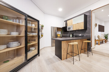 Modern style kitchen with wooden furniture combined with black, a counter with stools and a sideboard for dishes with sliding glass doors