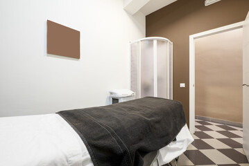 Room in an aesthetic medicine center with a stretcher to lie down and apply treatments and a shower cabin with a screen to remove the oils