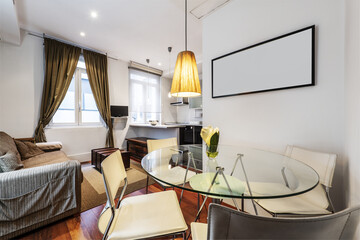 Living room of a house with eclectic-inspired furniture, a sofa with many cushions, a circular glass table and a reddish wooden floor