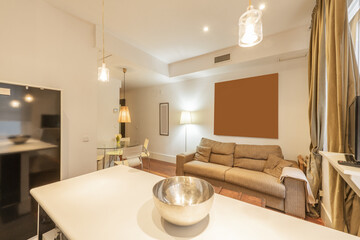 Living room of a house with eclectic inspired furniture, a gray fabric sofa, a circular glass dining table and a reddish wooden floor, a sideboard with a white top and an empty metal bowl