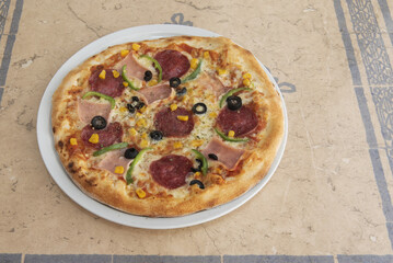 A pepperoni pizza with peppers, ham and sweetcorn with black olives prepared in a kebab restaurant