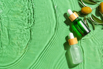 Bottles of essential olive oil in water on green background