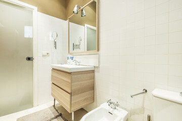 Bathroom with white porcelain sink, chrome faucets, mirror with wooden frame and tempered glass door