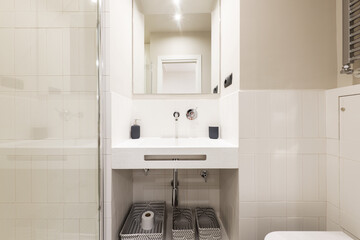 Bathroom with unusual design sink, chrome faucet and heated towel rail, frameless mirror, fabric baskets under sink and tempered glass glass partition