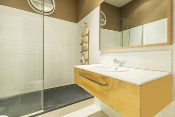 Bathroom with a suspended drawer unit with a marble countertop and a built-in sink under a mirror with a wooden frame and a shower cabin with a tempered glass screen