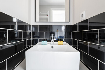 Bathroom with square white porcelain sink with black tiles and square mirror with black frame