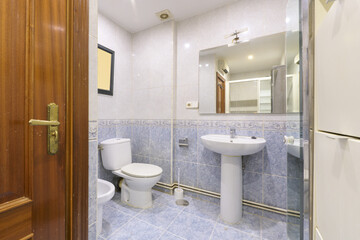 Fototapeta na wymiar old-fashioned bathroom with frameless mirror on the wall and blue tiles half up to match the floor