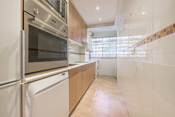 Elongated kitchen with wooden furniture, white countertops, cement latticework and integrated appliances