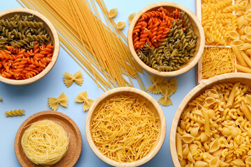 Bowls with different types of raw pasta on light background