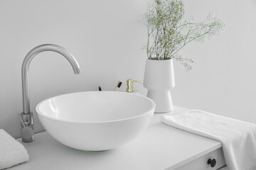 Sink and vase with flowers on table in light bathroom
