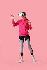 Sporty young woman in VR glasses on pink background