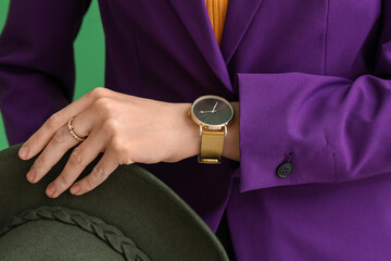 Woman with stylish wristwatch and hat on green background, closeup