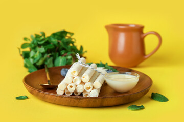 Board with delicious wafer rolls, condensed milk, blueberries and mint on yellow background