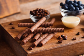 Board with delicious chocolate wafer rolls, condensed milk and blueberries on brown wooden table