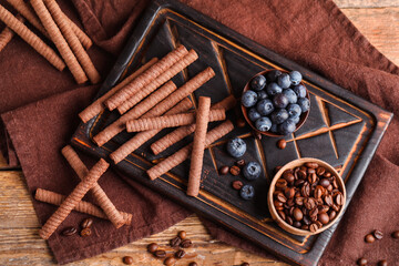 Board with delicious chocolate wafer rolls, blueberries and coffee beans on brown wooden table
