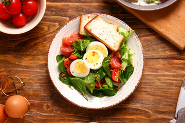 Plate of delicious salad with boiled eggs and salmon on brown wooden background