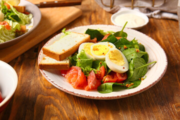 Plate of delicious salad with boiled eggs and salmon on brown wooden background