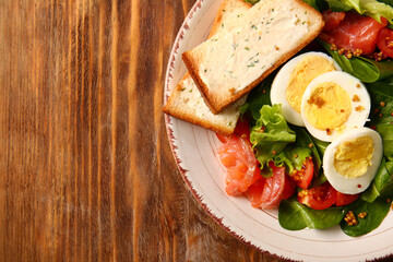Fototapeta na wymiar Plate of delicious salad with boiled eggs and salmon on brown wooden background