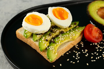 Delicious avocado toast with boiled egg on black plate, closeup