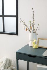 Vase with tree branches, Easter eggs and rabbit on table near grey wall