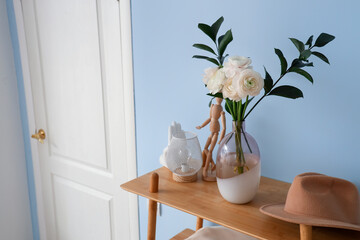 Vase with ranunculus flowers, mannequin, lamp and hat on shelf in hall