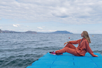 Fototapeta premium A woman tourist looks at the mountains and the sea in an orange sports suit, jacket and backpack. Hiking with family. Great view of nature. Travel agency. High quality photo