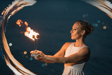 Caucasian woman dancing with fire in the water. Fire show at sea. Acrobatics on the beach. Yoga and...