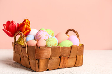 Wicker basket with painted Easter eggs and tulip flowers on white table near pink wall