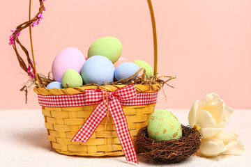 Wicker basket with painted Easter eggs and tulip flowers on white table near pink wall