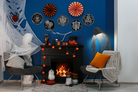 Jack-o'-lanterns and different Halloween decorations on black fireplace near blue wall